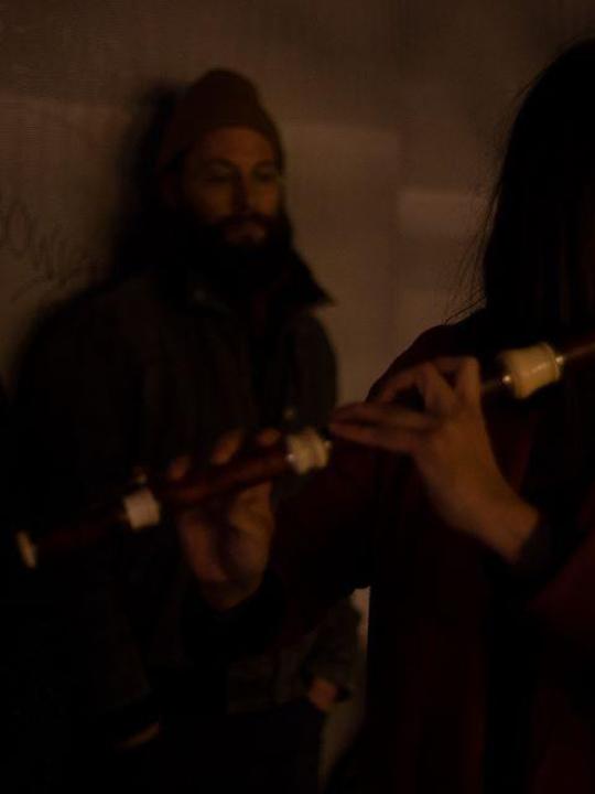 Violeta Motta performing solo: standing before two spectators in dim light, intimate setting with soft shadows and focused posture