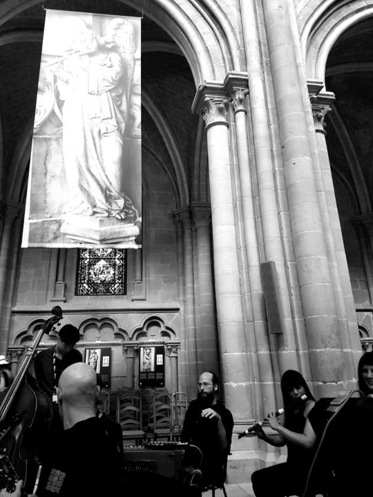 Violeta Motta and other musicians playing in a church: ensemble seated and standing amid pews and arches