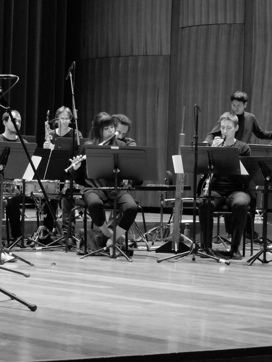 Violeta Motta performing in an orchestra: seated with fellow musicians, playing traverso amid orchestral scores