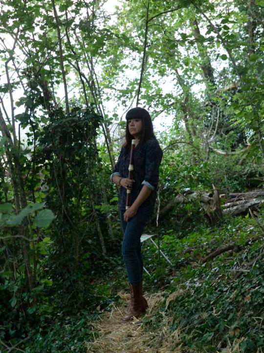 Violeta Motta with her traverso in the forest: standing beneath the trees, holding the traverso at her side