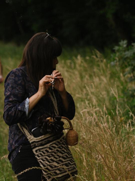 Violeta Motta with her piccolo in a field: standing in tall grass, playing the piccolo