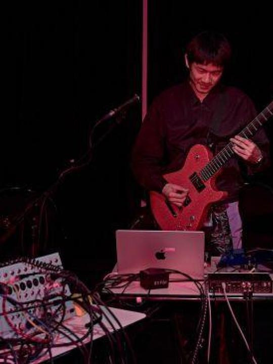 Portrait of Sikai Li with his guitar and his computer: black and red