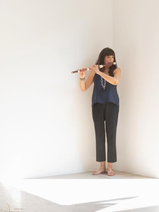 Violeta Motta playing the traverso: standing in a white environment, full-body view, holding the wooden flute at performance posture, soft even lighting